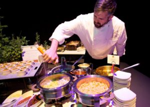 Kaspars Catering Chef saucing and serving food at Macaroni Action station at Gala Event. Hors d'Oeurves in the background.